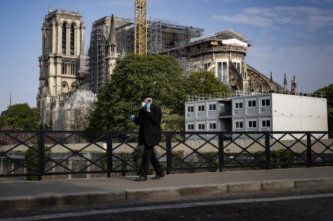 Un hombre con guantes protectores y mascarilla pasa junto a la Catedral de Notre-Dame ( París)