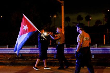 Police officers prevent people demonstrating in solidarity with protesters in Cuba from advancing on a highway, in Miami